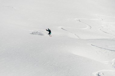 awesome beautiful view of a snow-covered mountain slope with traces of a snowboard and a man on a snowboard speedly slides down on it. Freeride concept