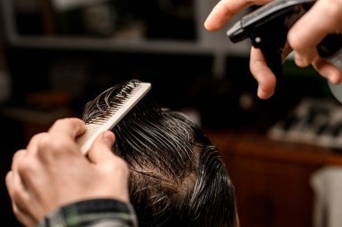 Selective focus on male client head with wet hair which barber masterfully combs. Hairdresser comb hair and make new style for his demanding client