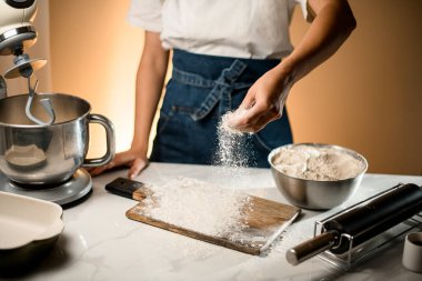 view on hand of woman pouring white flour on wooden cutting board on the table. Dough preparation process