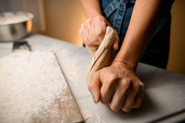 Close-up view on female hands kneading raw bread dough on wooden board. Preparation of the dough.
