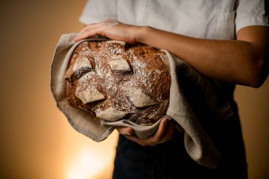delicious freshly baked rustic organic loaf of bread in hands of woman. Homemade bread food photography. Cropped photo. Close-up