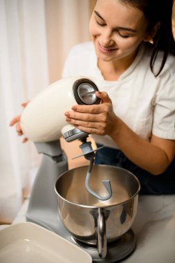 Close-up view on kitchen machine mixer and young woman accurate setting it up. Modern kitchen appliances