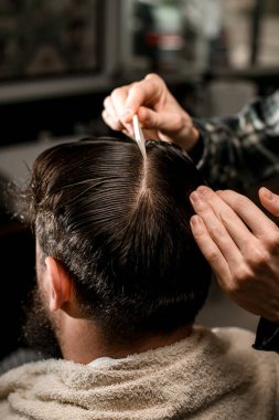Close-up view of male client head which barber combs and divide into sections. Hairdresser comb hair and make new style for his demanding client