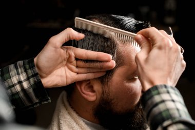 close-up the hand of a male barber neatly holds a strand of wet male hair and skillfully combs it with a comb