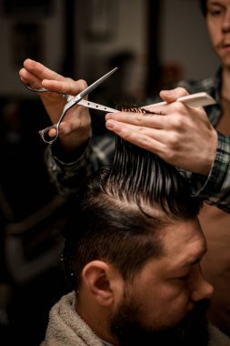 close-up of male hands of a barber holding a strand of hair and scissors and masterfully do a haircut. Professional barber make haircut of his client clipart