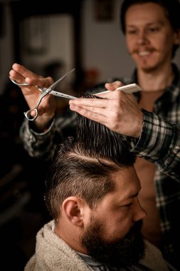 focus on male hands of a barber holding a strand of hair and scissors and do a haircut. Professional barber make haircut of his client