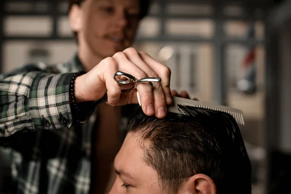 selective focus on hand of man barber with hair scissors and comb neatly combing the wet hair of a male client. Barbershop