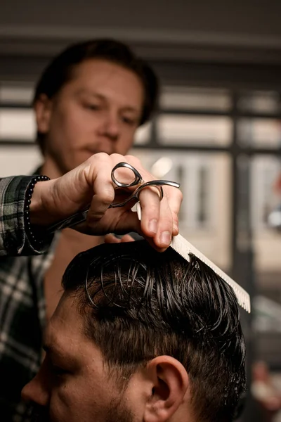 selective focus on hand of man barber with hair scissors and comb accurate combing the wet hair of a male client. Barbershop
