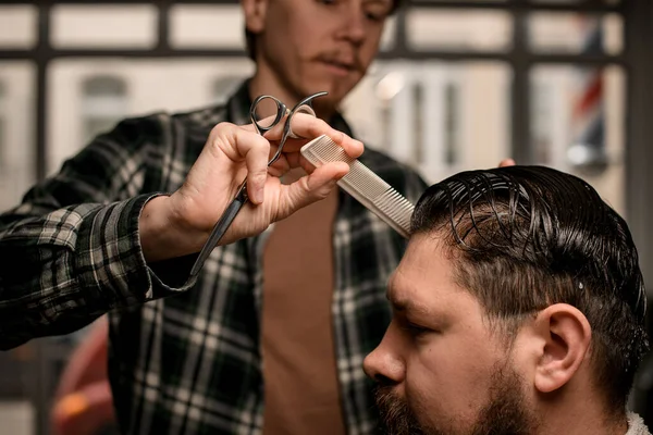 Close-up view of hand of man barber with hair scissors and comb neatly combing the wet hair of a male client. Barbershop