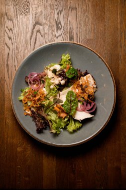 Mantarlı salata ve taze yeşil ve mor marul yaprakları ve havuç ve pancar yaprakları ve tabakta kırmızı soğan halkaları.