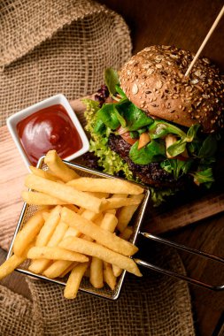 Büyük, lezzetli, çift katlı burger, patates kızartması ve ahşap masada ketçap üzerine yakın plan harika bir manzara.
