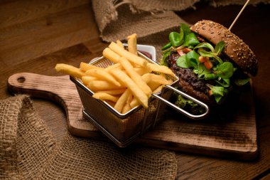 Patates kızartmasının iştah açıcı manzarası ve ahşap tahtanın üzerinde taze marul ve ıspanakla birlikte büyük lezzetli çift burger.
