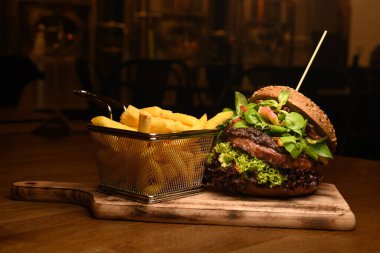 Taze marul, ıspanak, patates kızartması ve ahşap tahtayla harika bir çift burger manzarası.