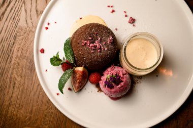 Tabakta yakın plan çikolatalı pasta, dondurma topu, taze ahududu ve incir ve bir kavanoz krema.