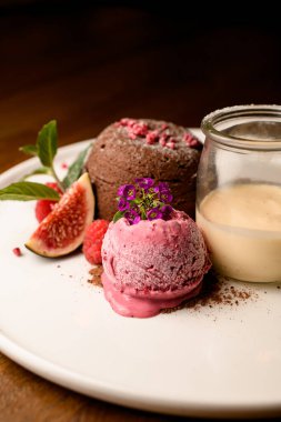 Beyaz tabakta çiçekle süslenmiş dondurma topuna odaklanın. Çikolatalı pasta ve kavanozdaki kremayla süslenin.