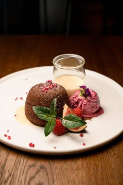 Dondurma toplu çikolatalı pasta, taze ahududu, incir ve beyaz tabakta servis edilen bir kavanoz krema.