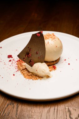 Bisküvi parçacıklarıyla süslenmiş beyaz çikolata küresinin tatlı tatlısına ve tabaktaki siyah çikolatayla dondurmaya bak.