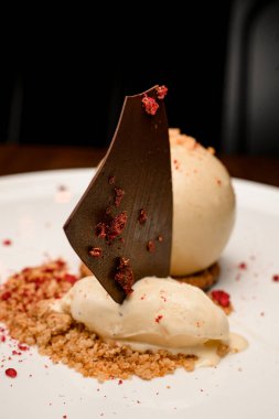 Bir dilim siyah çikolata ve tabakta bisküvi parçacıklarıyla süslenmiş beyaz çikolata küreli dondurmaya odaklan.