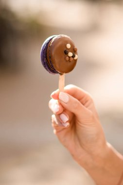 Kafkas kadın eli parmaklarıyla nazikçe tutuyor. Arka planda bulanık bir çubuğun üzerinde çikolata kremalı lezzetli bir makaron. Lezzetli tatlı