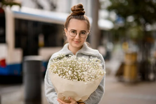 Charming young woman with large bouquet of white gypsophila flowers in wrapping paper in the hands