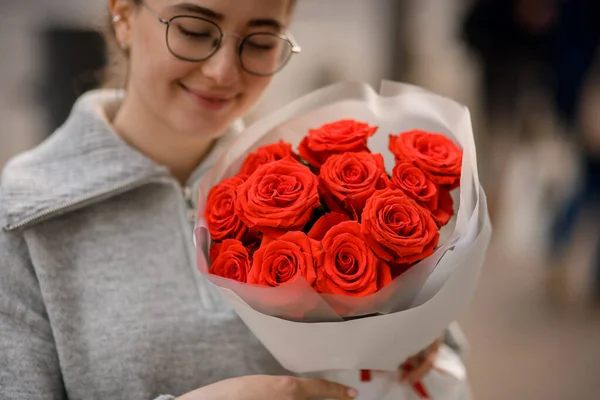幸せなハンサムな若いです女性とともに花束の明るい赤いバラで包み紙で彼女の手 — ストック写真