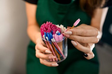 Parlak renkli tek kullanımlık kirpik fırçaları ve kadın ellerinde pamuk tomurcukları olan kutulara yakın çekim. Bulanık arkaplan