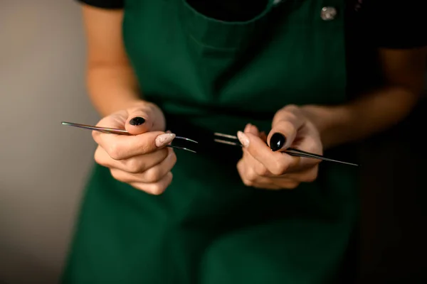 close-up of the female hands of the master beautician holding steel tweezers. Cropped photo. Blurred background.