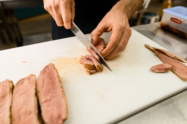 白いキッチンボードにナイフで焼き肉をスライスシェフの手のクローズアップ写真 — ストック写真