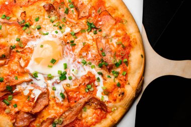 Pastırmalı, yumurtalı, peynirli ve otlu sıcak pizza, masanın üzerindeki tahta tahtaya yakın plan. Yukarıdan dikey üst görünüm