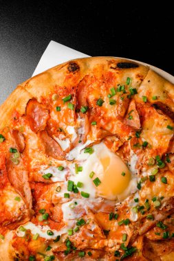 Prosciutto, yumurta ve yeşil soğanlı sıcak pizza. Siyah arka planda kahvaltı pizzası, üst manzara.