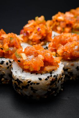 Siyah zemin üzerinde susamlı ve karamelize soğanlı taze yapılmış suşi rulosu. Dikey fotoğraf.