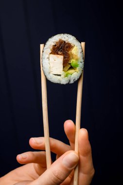 Mans el ele suşi rulo füme yılan balığı, avokado, salatalık ve peynir ile koyu arkaplanda çubuklar