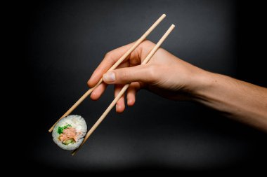 Ton balığı, krem peynir, avokado, salatalık ve yeşil buzağıdan yapılmış bir parça makarna. Siyah arka planda bambu çubukları var..