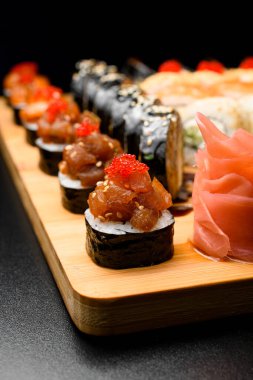 Masadaki tahta servis masasında somon ve tobiko buzağı ile maki rulolarının yakın plan fotoğrafı. Bulanık arkaplanda rulo kümesi.