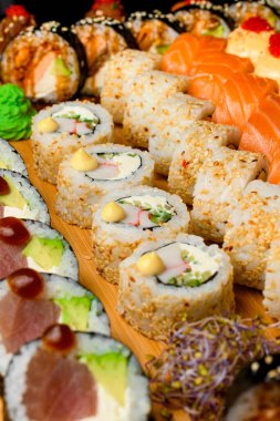 Japon yemek afişi: ahşap kesme tahtasının üzerinde farklı rulo setleri. Somon, sebze, tobiko buzağı, peynir, susam ve suşi ruloları.