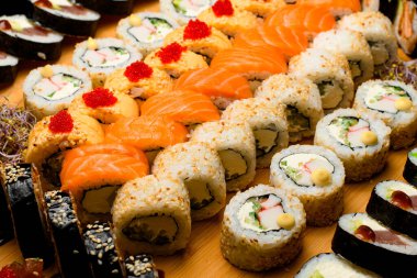 Tahta kesme tahtasının üzerinde rulo var. Somon, sebze, tobiko buzağı, peynir, susam ve suşi ruloları.