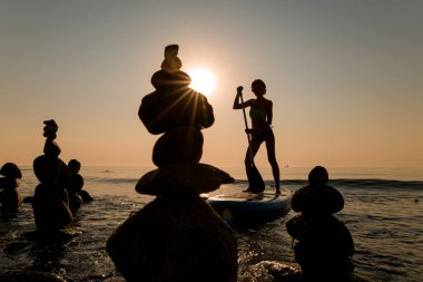 Sörf tahtasının üzerinde yüzen hassas kızın silueti. Ön planda taştan kule.
