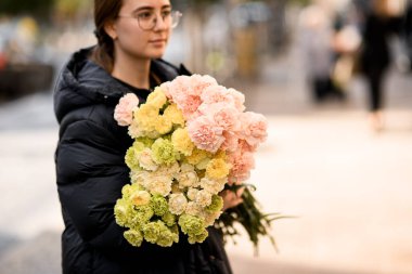 Kadınların elinde büyük bir buket sarı, pembe, limon ve süt rengi karanfil. Önemli bir olay için mevcut. Yakın görünüm.