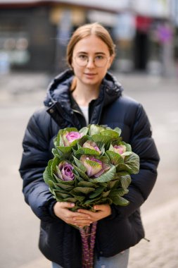 Gülümseyen genç kadın elinde kocaman bir demet güzel lahana buketi tutuyor. Çiçek düzenlemeleri için ekin