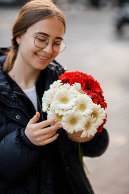 Elinde bir buket taze Gerbera çiçeğiyle gülümseyen güzel bir kadın. Arka plan bulanık. Yakın plan.