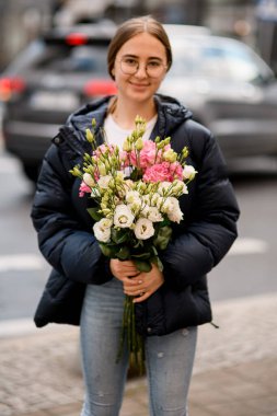 Gülümseyen genç kadın elinde çiçek buketi tutuyordu. Krem rengi, pembe ve sarı renkli çiçek çiçekleri.