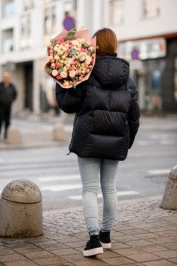 Büyük, güzel bir buket pembe, sarı ve süt gülleri. Kadınların omuzlarında okaliptüs dalları var. Arka plan