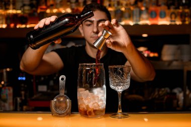 Şeffaf bardakları buz küpleriyle karıştırıp tezgahın üzerinde cam bardakları içiyorlar ve barmen jigger 'ın karışımına bir madde ekliyor.