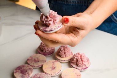 Şef kadının makarnaların yarısına pembe meyve ganache kremi sıkarken çekilen yatay çekimini kapat. Ev pastası konsepti