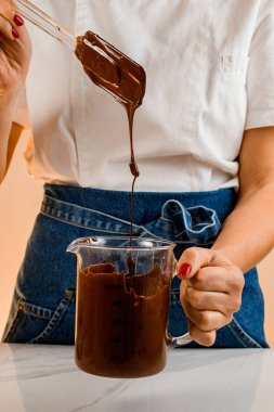 Aşçı kadın eritilmiş çikolatayla fıstığı spatula kullanarak ölçü kabında karıştırıyor. Tatlılar veya kekler için yemek malzemelerinin işleyişi