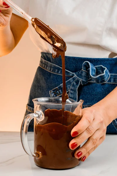 stock image Woman mixes melted chocolate and peanuts in transparet measuring cup using cooking spatula. Cooking process