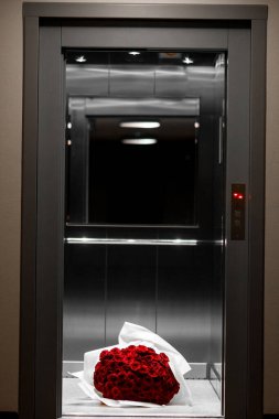 Asansör zemininde beyaz ambalaj kağıdına sarılı büyük bir buket kırmızı gül. Sevgili kız için beklenmedik bir hediye.