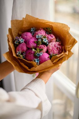 Bej ambalaj kağıdında çiçek açan taze pembe şakayık buketi tutan genç bir kadın. Gelin buketi