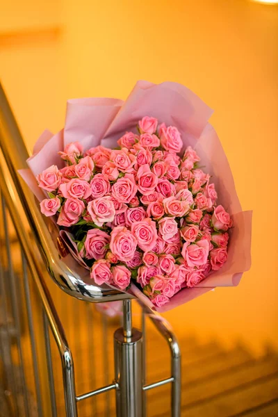 Stairwell with strikingly beautiful large bouquet of fresh roses in pink wrapping paper. Flovers delivered by courier. Gift dedicated to a special date.