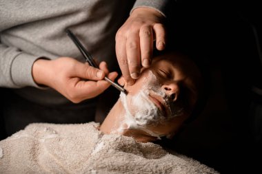 Müşteri berber koltuğunda oturup erkek berbere tıraş olurken rahatlıyor. Kişisel bakım teması